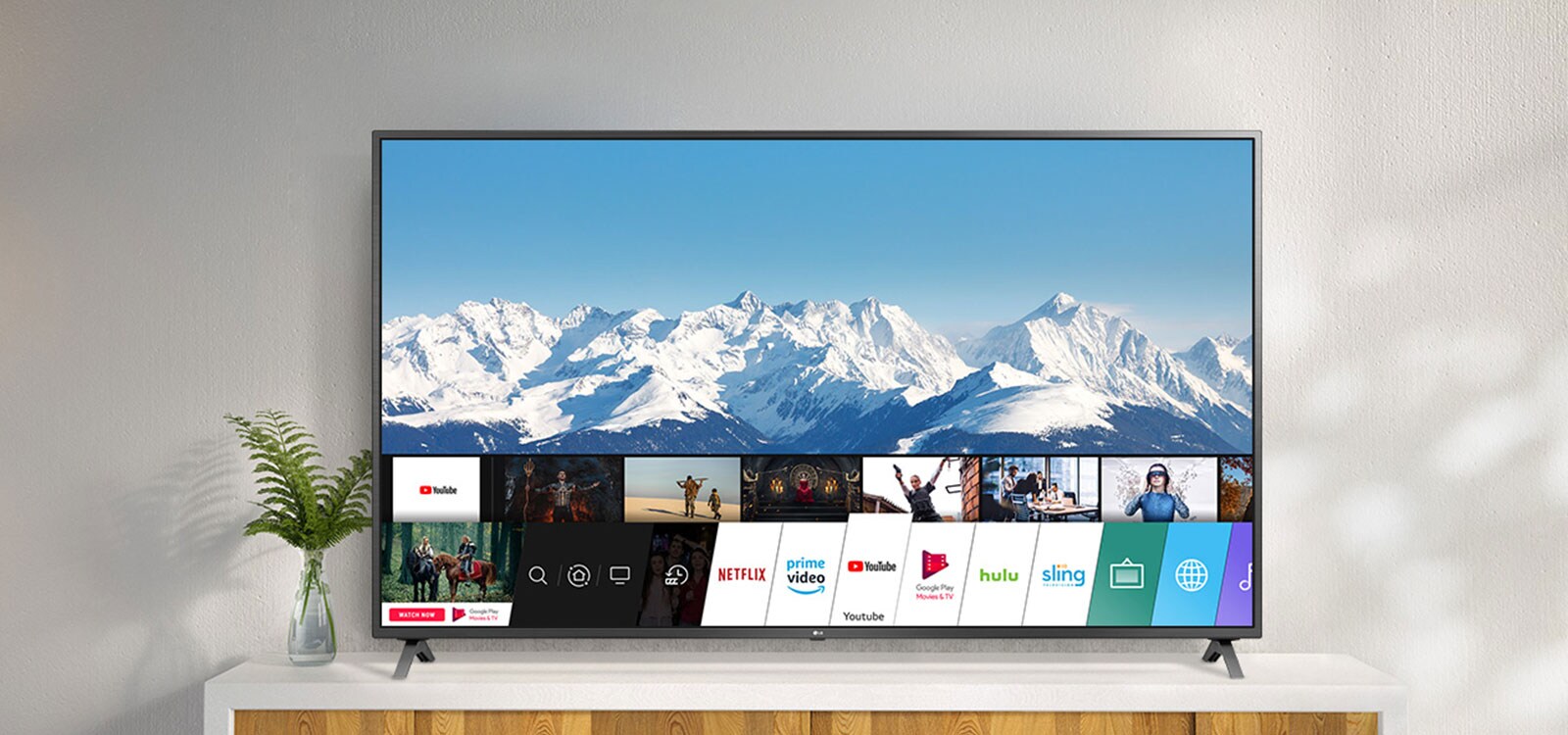 Televizor stojící na bílém stojanu proti bílé zdi. Televizní obrazovka s úvodní obrazovkou se systémem webOS.