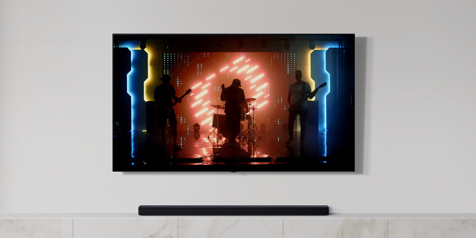 Bílý obývací pokoj s TV a soundbarem. Na TV obrazovce je hudební skupina, hudebníci hrají na nástroje a zpívají. (přehrát video)