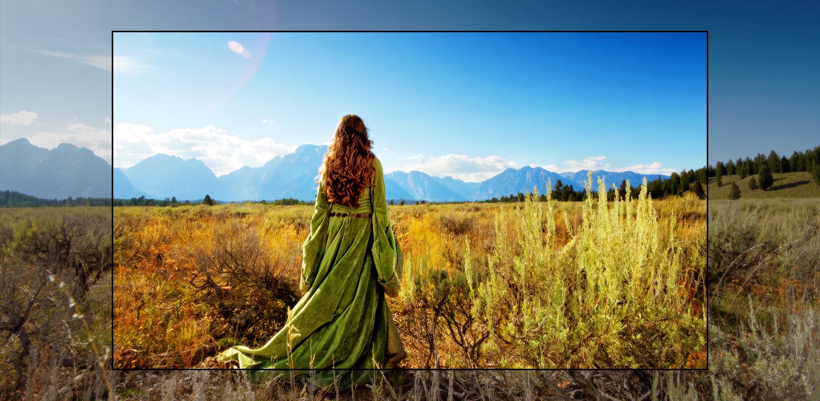 Televizní obrazovka se scénou z fantasy filmu, ve kterém v polích stojí žena čelem k horám.