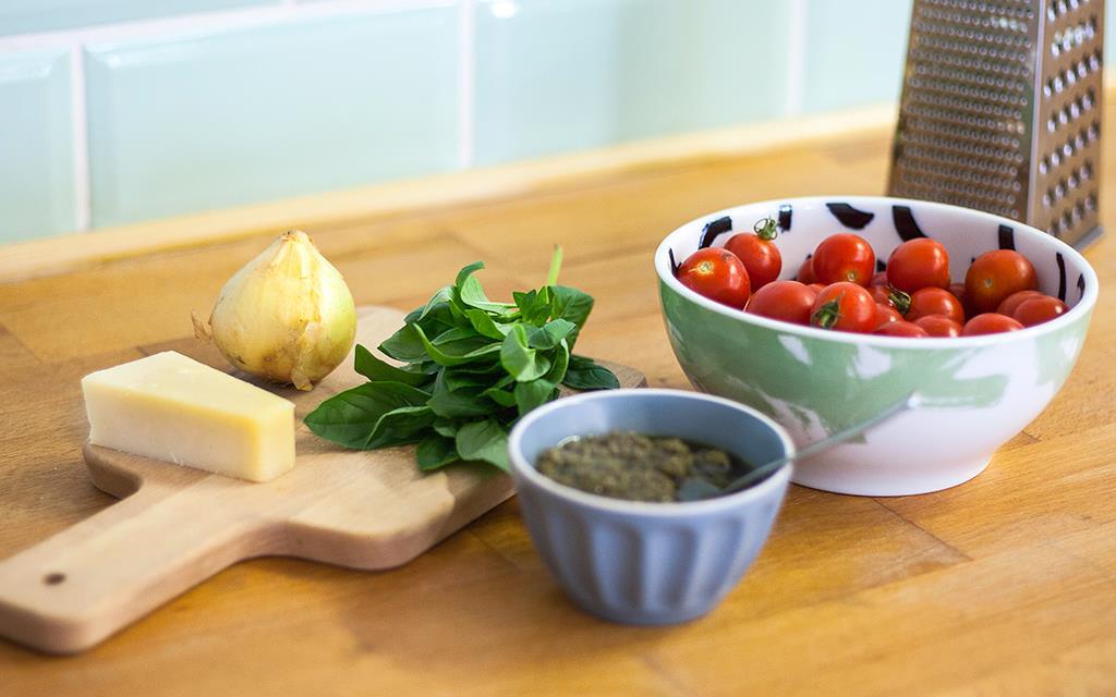 Frontansicht verschiedener frischer Zutaten für einen Tomaten-Quiche mit Parmesan, Basilikum, Zwiebeln, Kirschtomaten und Pesto