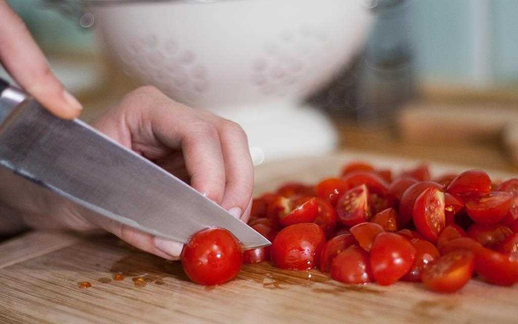 Ansicht einer Person, die Kirschtomaten mit einem Küchenmesser schneidet