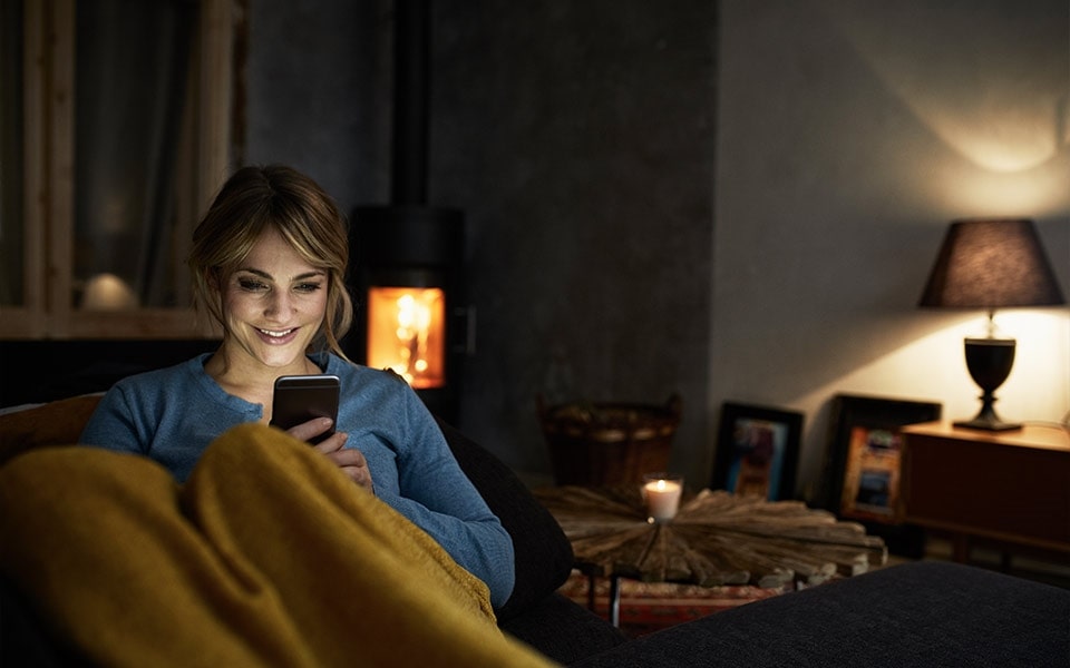 A smiling woman looks at her smartphone while relaxing in a cosy living room