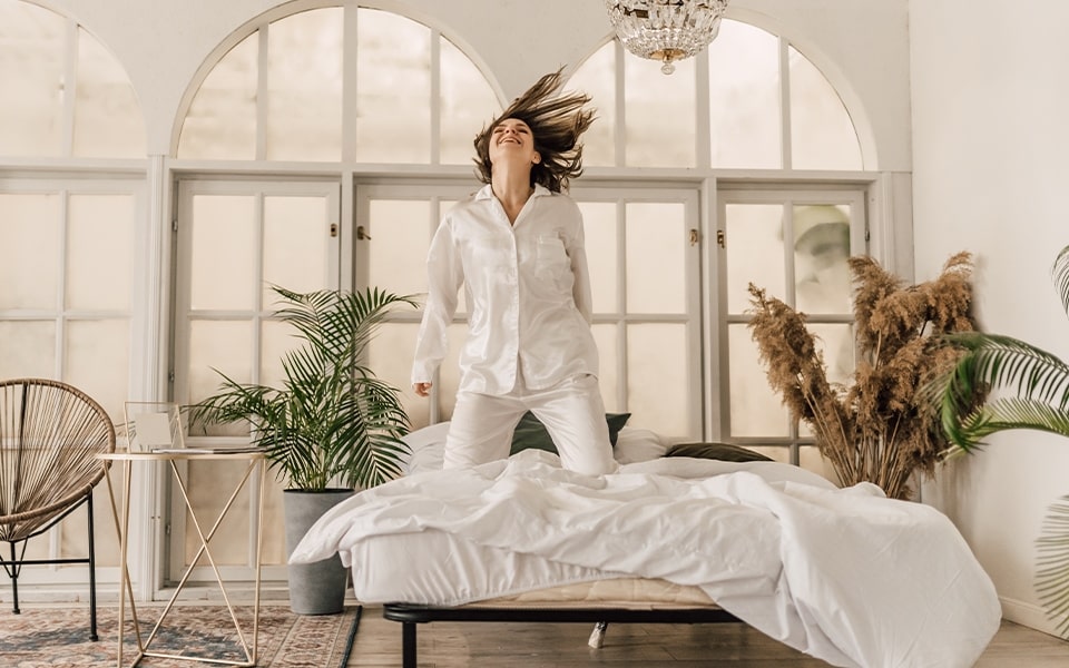 A woman jumps on a bed of freshly steam-cleaned linens.