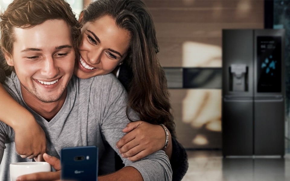 A couple looking at a smartphone screen with a refrigerator in the background