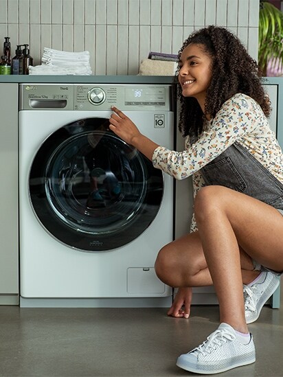 Ein Bild eines jungen Mädchens, das auf ihre neue LG-Waschmaschine sitzt und zeigt.