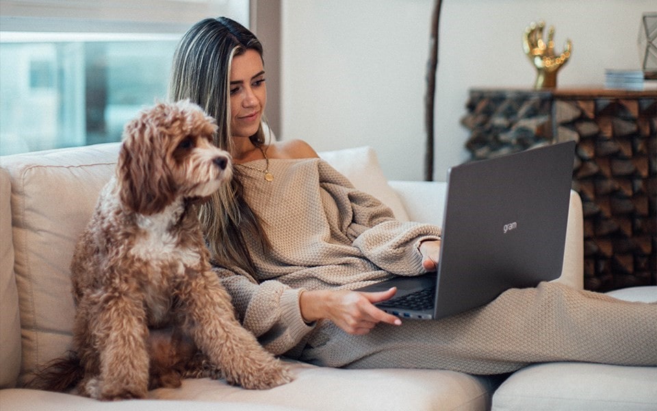 Eine Frau sitzt auf einem Sofa mit ihrem Hund und einem Laptop auf dem Schoß