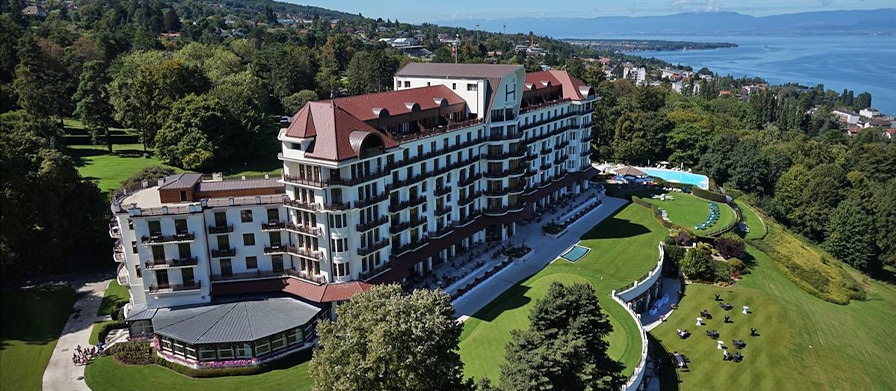 Das Hotel Royal, Evian Resort aus der Vogelperspektive mit Blick auf Bäume und ein Gewässer.