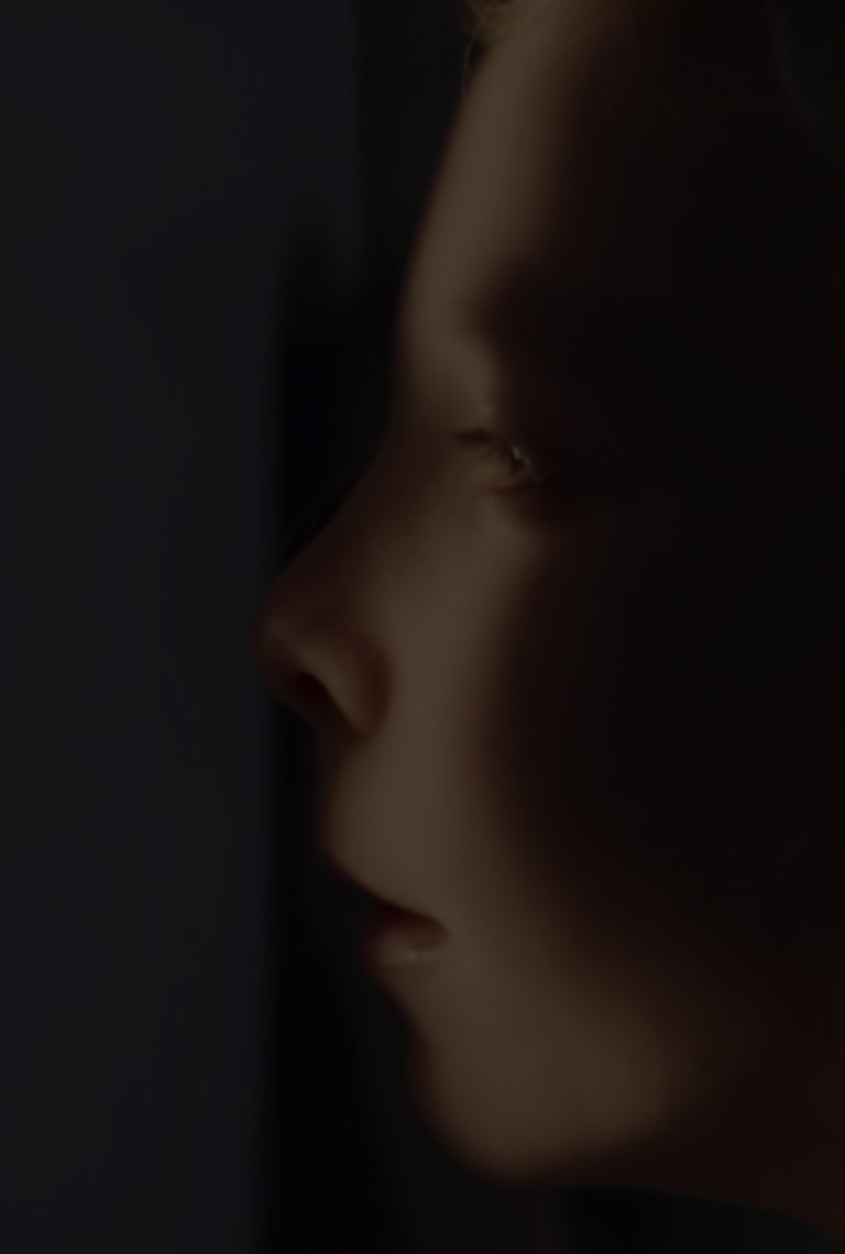 Eine Nahaufnahme vom Gesicht eines Mädchens, das sich zum Teil im Schatten, zum Teil im Licht befindet, während es aus seinem Versteck blickt.