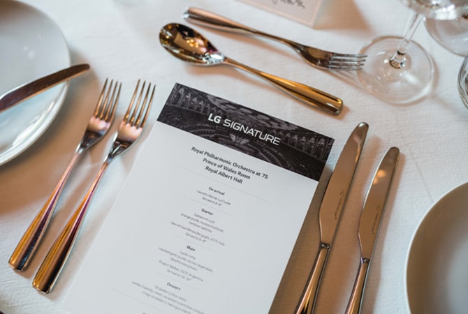 Eine Speisekarte mit der Überschrift „LG SIGNATURE” liegt auf einem weißen Tischtuch mit einem Gedeck für gehobene Küche.