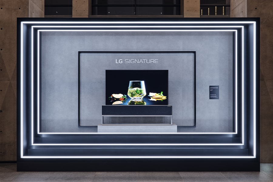 Eine Illustration des LG SIGNATURE OLED R, umgeben von Betonwänden mit drei Schichten. Der Fernsehbildschirm in der Mitte zeigt einen roten Sonnenuntergang.