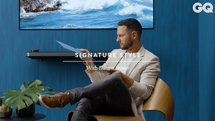 Darren Palmer sitzt auf einem Stuhl und liest ein paar Informationen vor dem lg signature OLED TV W, das an die blaue Wand gehängt wurde