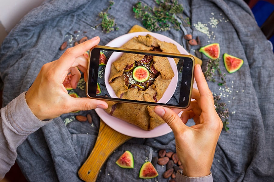 Hände mit einem Smartphone über einem Feigenkuchen beim Fotografieren des Tellers.