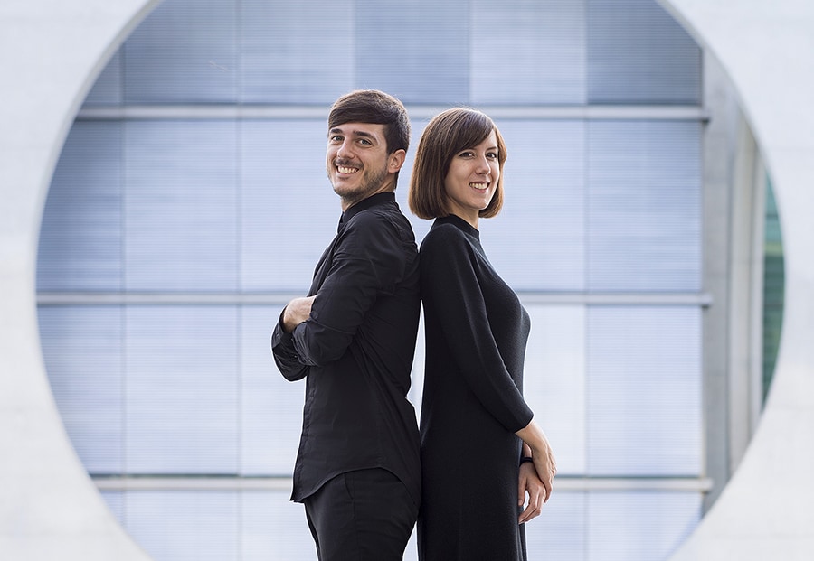 Die Künstler Anna Devis und Daniel Rueda stehen Rücken an Rücken und lächeln