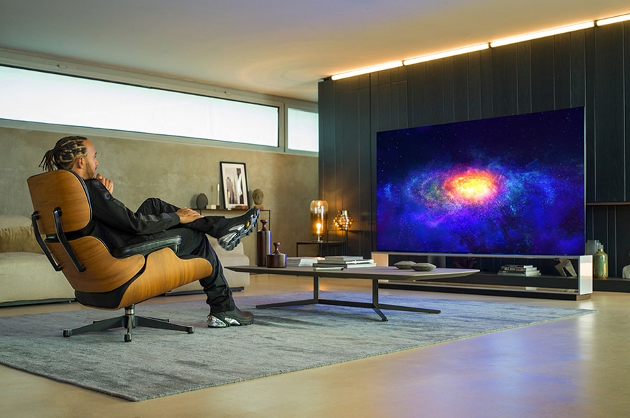 Lewis Hamilton sitzt auf einem Sofa und sieht auf dem LG SIGNATURE OLED 8K ZX TV fern.