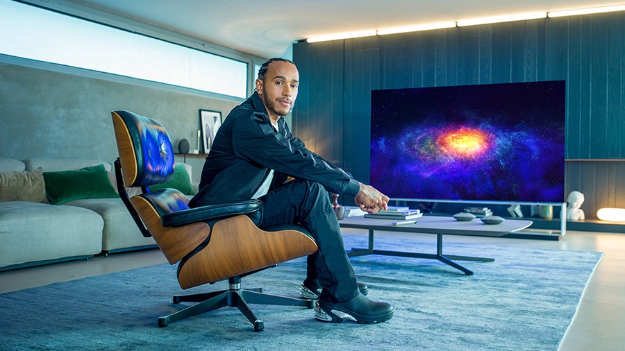 Lewis Hamilton sitzt auf einem Sofa, hinter ihm ist der LG SIGNATURE OLED 8K TV zu sehen.