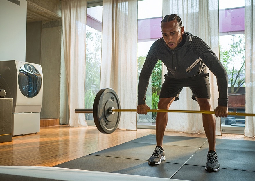 Lewis Hamilton trainiert in einem seiner Wohnräume, neben ihm steht der LG SIGNATURE TWINWash™ Waschtrockner.