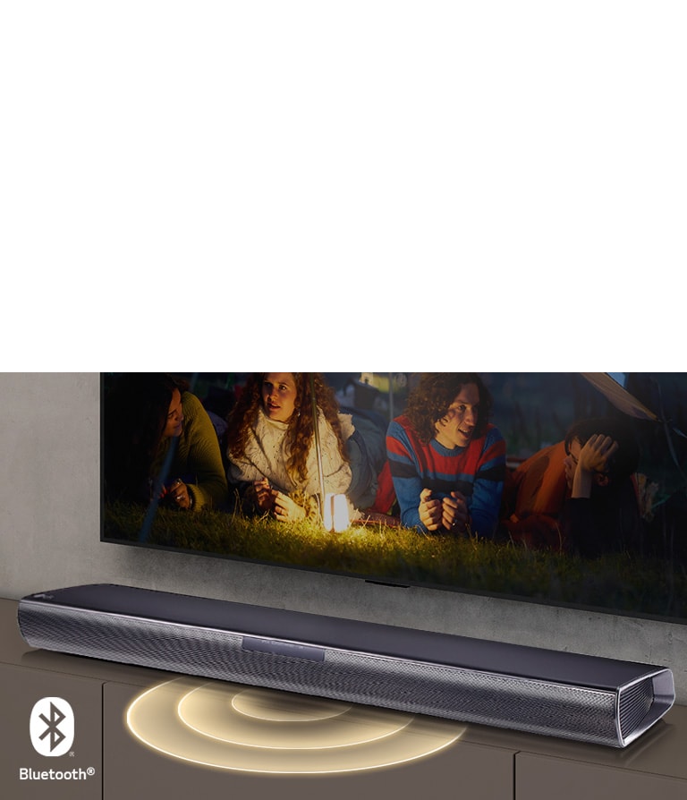 LG TV hænger på væggen, og på skærmen viser det 2 par liggende på græsset. Foran dem er der en lampe. En LG Soundbar er under et LG TV. Lydgrafik kommer ud fra forsiden af soundbaren. Bluetooth-logoet vises i nederste venstre hjørne af billedet.