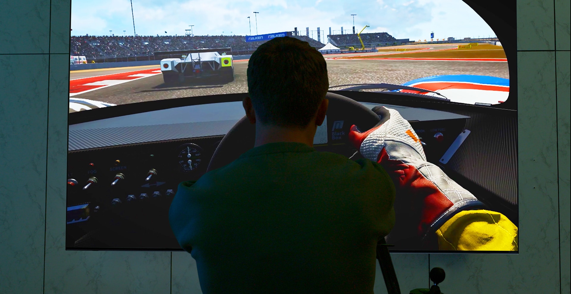 En mand sidder på et racersæde foran et stort fjernsyn og spiller et racerspil