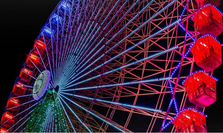 Grande roue légèrement décolorée s'illuminant la nuit, avec des étincelles de couleur se déplaçant sur l’écran à partir du côté gauche. À mesure que les étincelles de couleur se déplacent, l'écran passe d'un état nuageux à des couleurs vives et lumineuses.