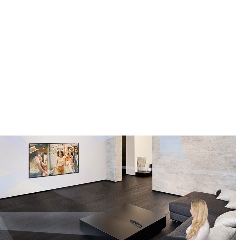 Une femme regarde des gens danser sur le téléviseur d’un grand salon au décor minimaliste.