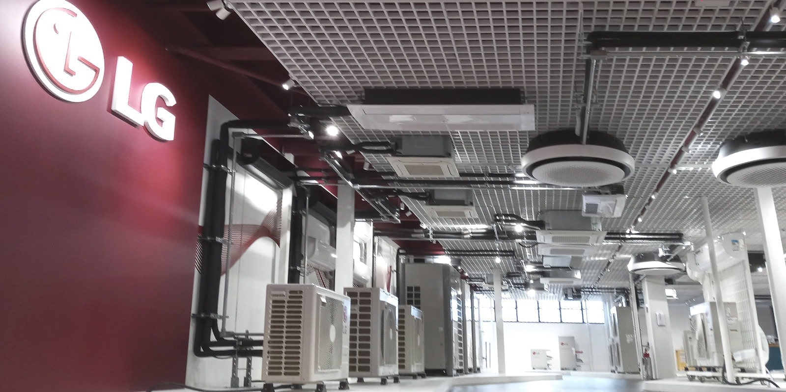 Dans une pièce semblable à une salle d'exposition, un grand logo LG orne le mur de gauche tandis qu'une série d'unités d’intérieur et d’extérieur LG agrémentent le plafond et le sol.