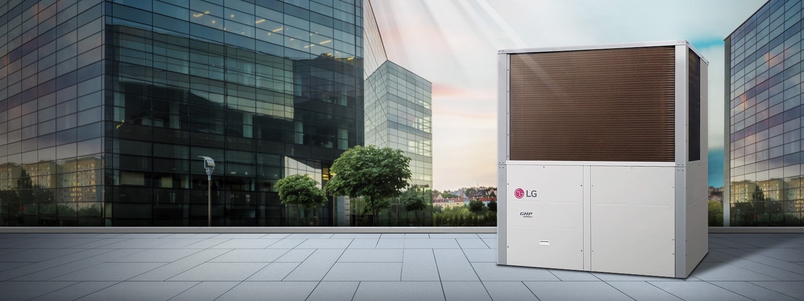 LG GAS Heat Pump GHP Super 3, with a silver frame, black top and white bottom, is showcased against a backdrop of glass buildings.