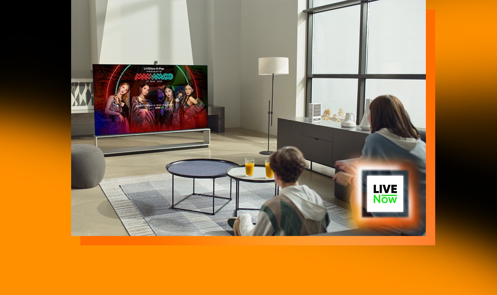 Deux personnes sont assises dans le salon et regardent la télévision. Une image d’accroche de Mamamoo apparaît sur l’écran du téléviseur. Un logo Livenow est placé dans le coin inférieur droit. 