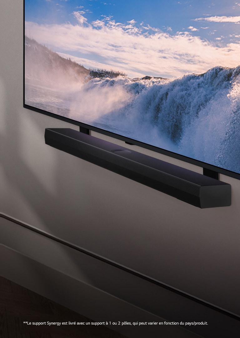 Le téléviseur LG TV et la Soundbar sont placés en biais, montés sur un mur. Sur le téléviseur, un gros plan d’une vaste cascade s’affiche, et la douce lumière du soleil tombe en cascade sur le mur, le téléviseur et la Soundbar. Un avis de non-responsabilité stipule ce qui suit : « Le support Synergy est livré avec un support à 1 ou 2 pôles, qui peut varier en fonction du pays/produit ».