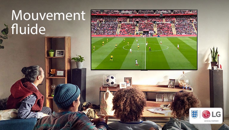 Quatre personnes assises sur un canapé regardent un match de football dans un salon.