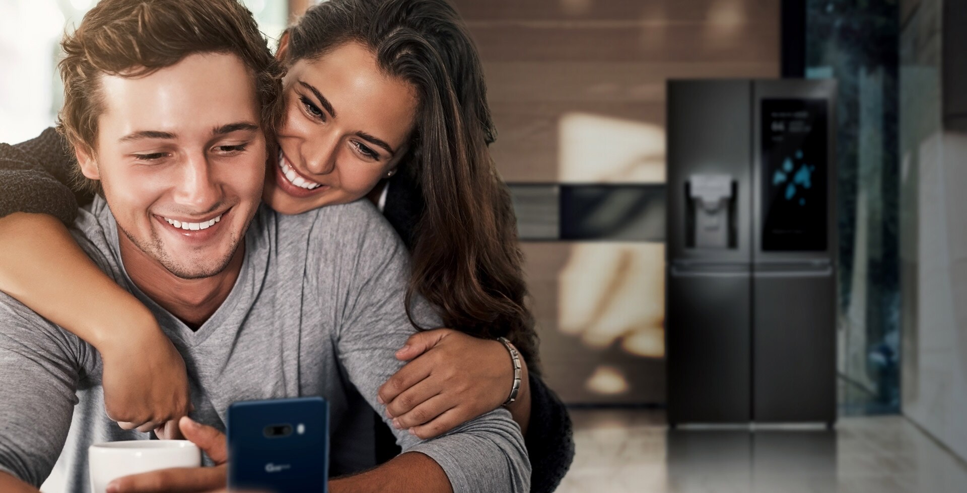 Un couple regarde un smartphone dans la cuisine avec un grand sourire.