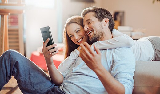 Le couple est enlacé et sourit tout en regardant le smartphone.