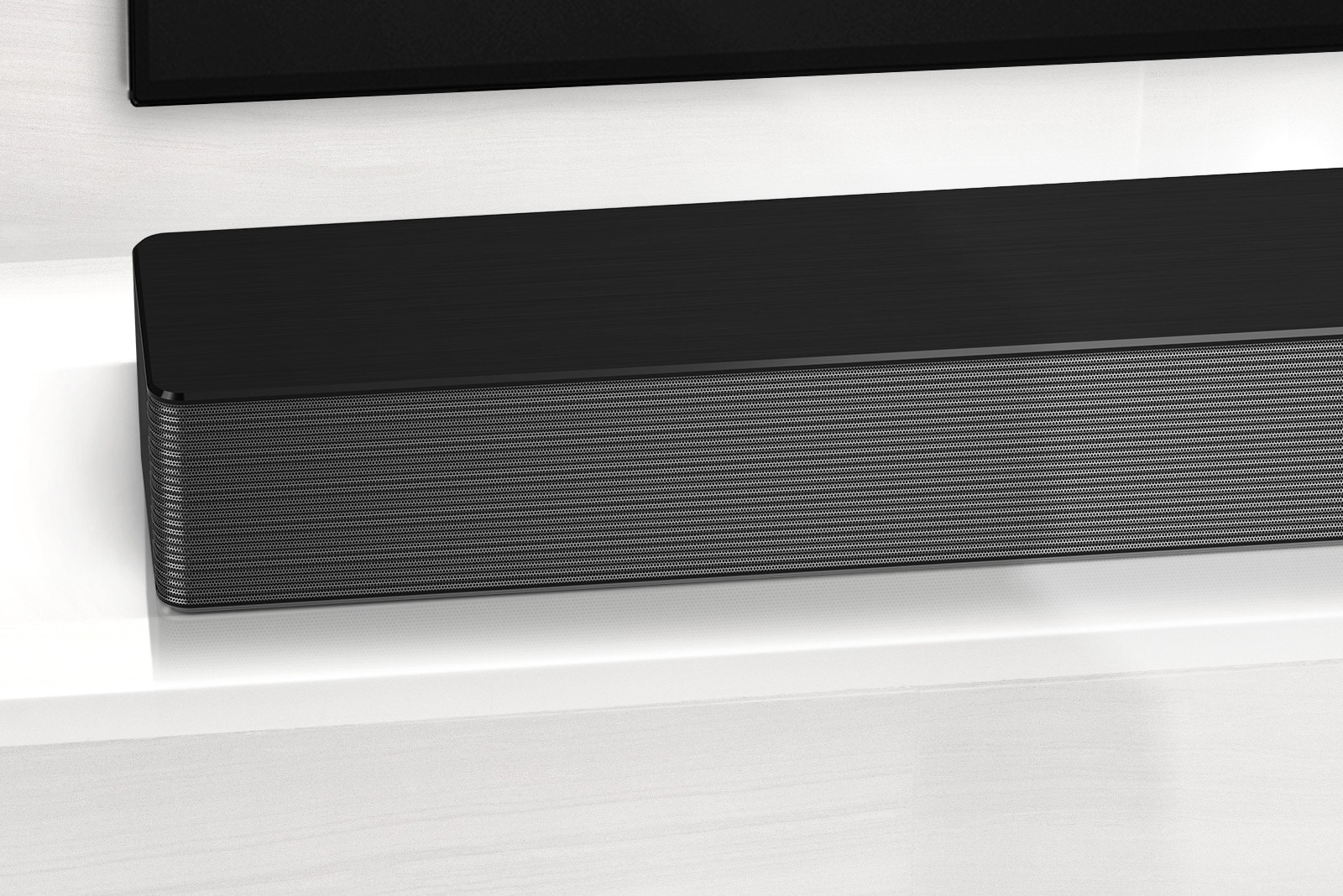 Close-up of LG Soundbar left corner. Bottom left side of TV is also visible. 