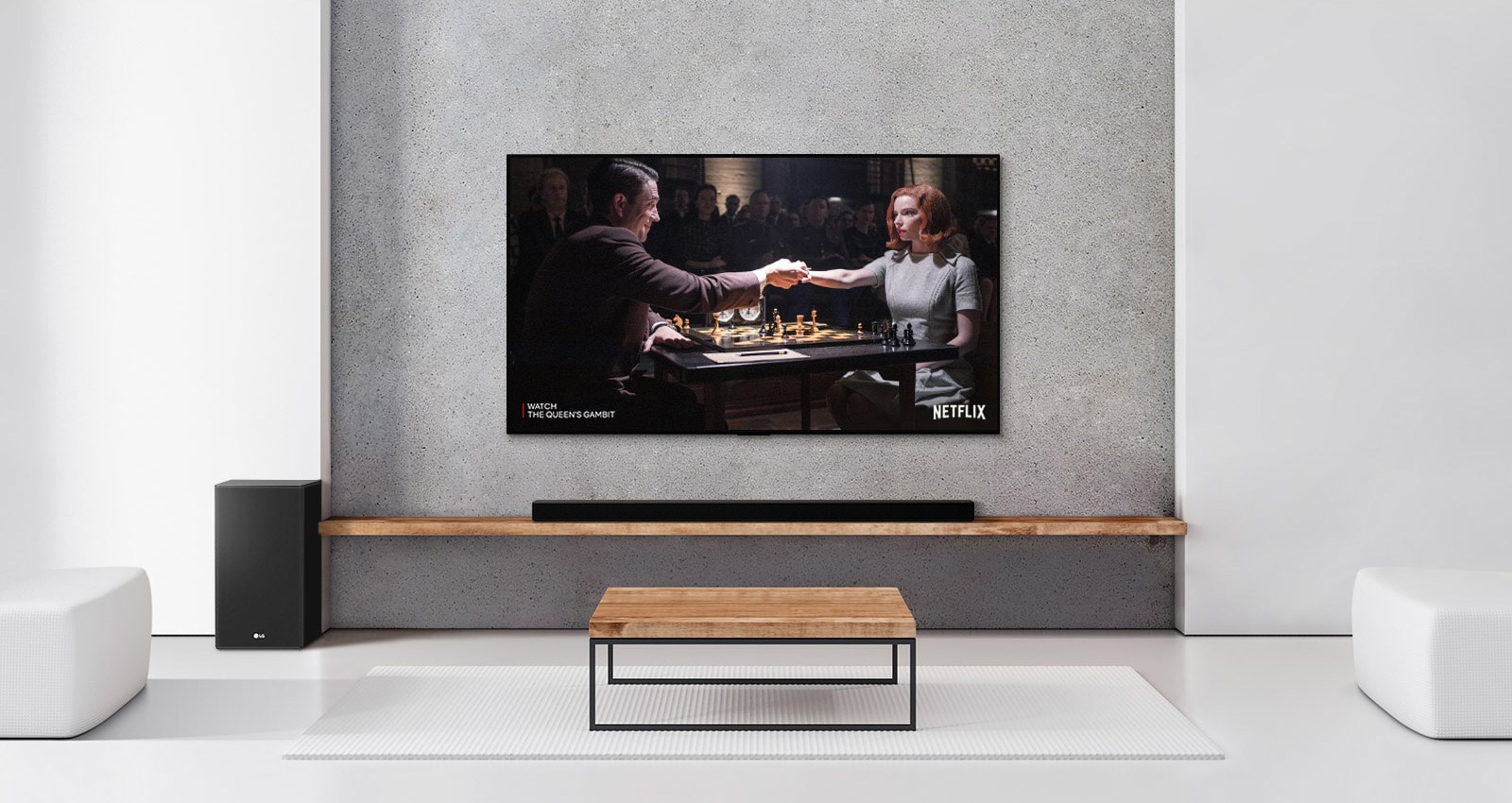 A subwoofer, and a soundbar, and TV are in a white living room. A woman and a man are playing chess on TV screen.