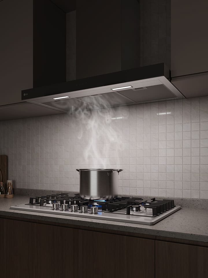 A built-in hood above a gas cooktop draws in steam rising from a pot while cooking in a modern kitchen.
