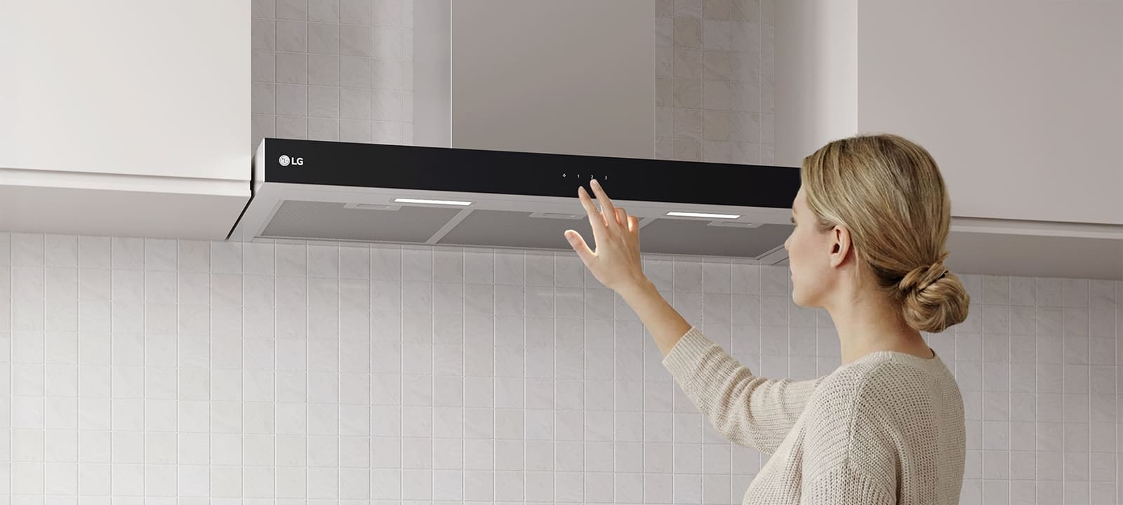 A woman adjusting the touch controls of a built-in hood above a cooktop in a modern kitchen with a white tile wall.