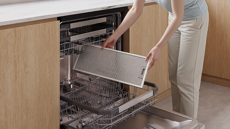 A person placing a removable grease filter from a range hood into a dishwasher for easy cleaning.