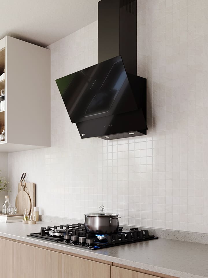 Modern kitchen interior featuring an angled glass hood above a gas cooktop with a pot, against a white tile wall.