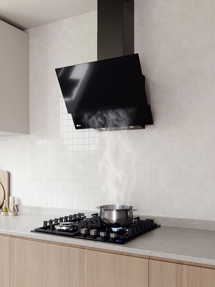 Modern kitchen interior featuring an angled glass hood above a gas cooktop with a pot, against a white tile wall.