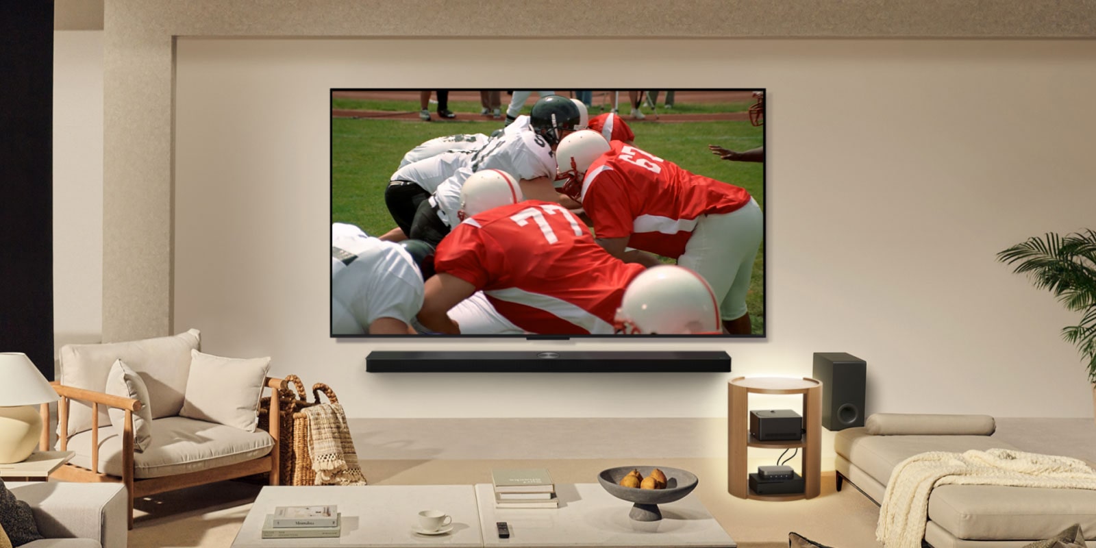Living room with an LG True Wireless TV on the wall. On the screen is an American football match. The TV setup also includes a wall-mounted LG Soundbar. And almost hidden from sight, the other peripherals are connected to a Zero Connect Box that is on a side table. The whole living room is neat, tidy, and has no wire-clutter.