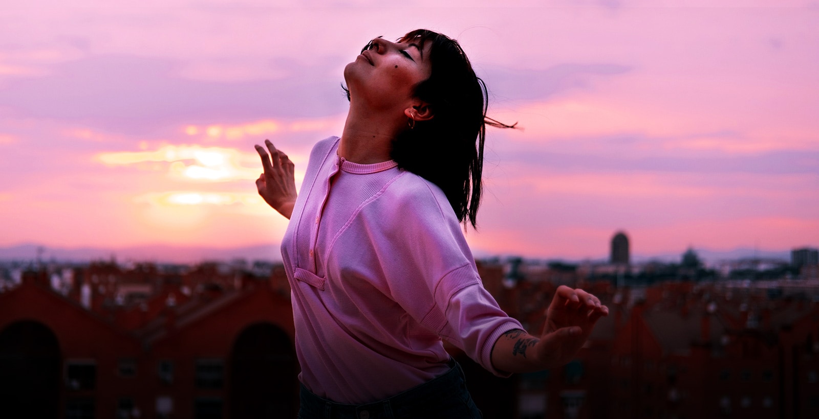 A bust shot of girl happily dancing on a roof at the magic hour
