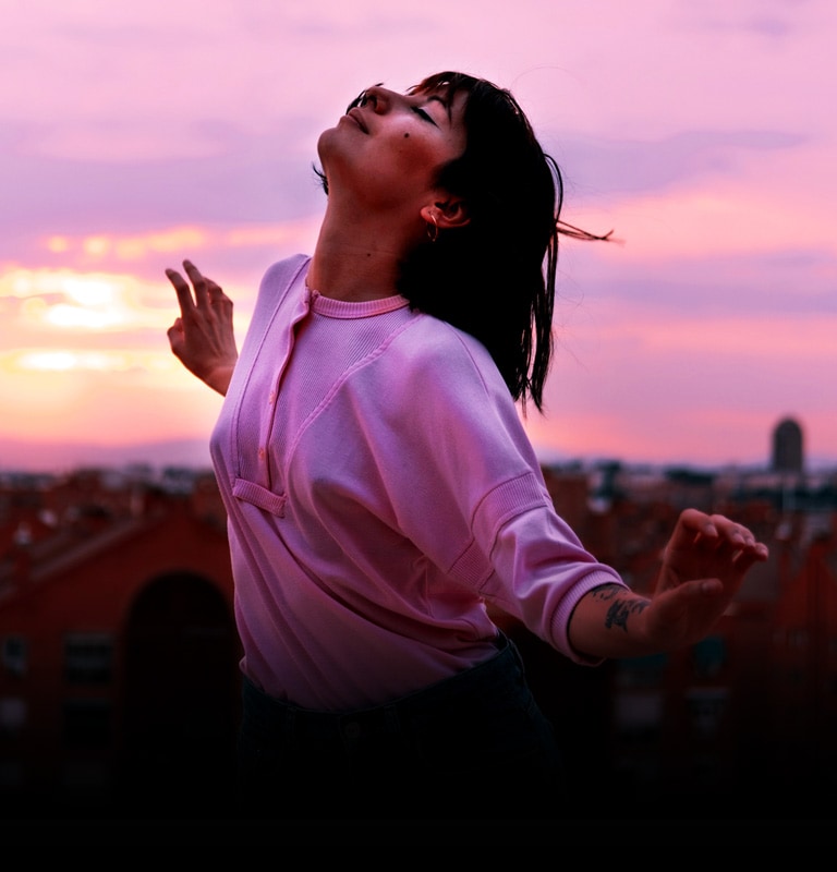 A bust shot of girl happily dancing on a roof at the magic hour