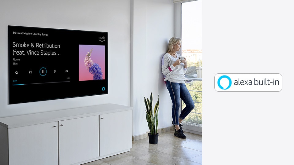 A woman is leaning beside TV, looking out the window and ask alexa about to play her favorite music.