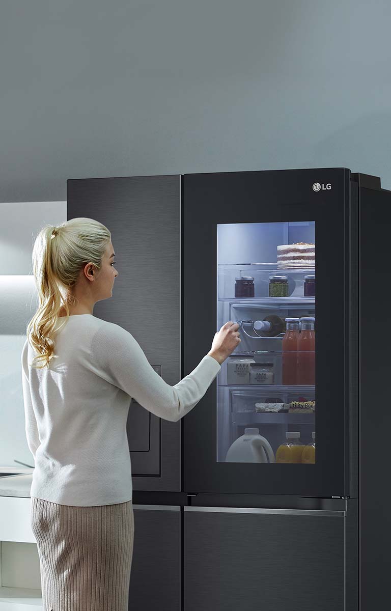 An image shows a woman at her InstaView refrigerator with knocking motion. The interior lights up and she can see the contents of her fridge without opening the door. 