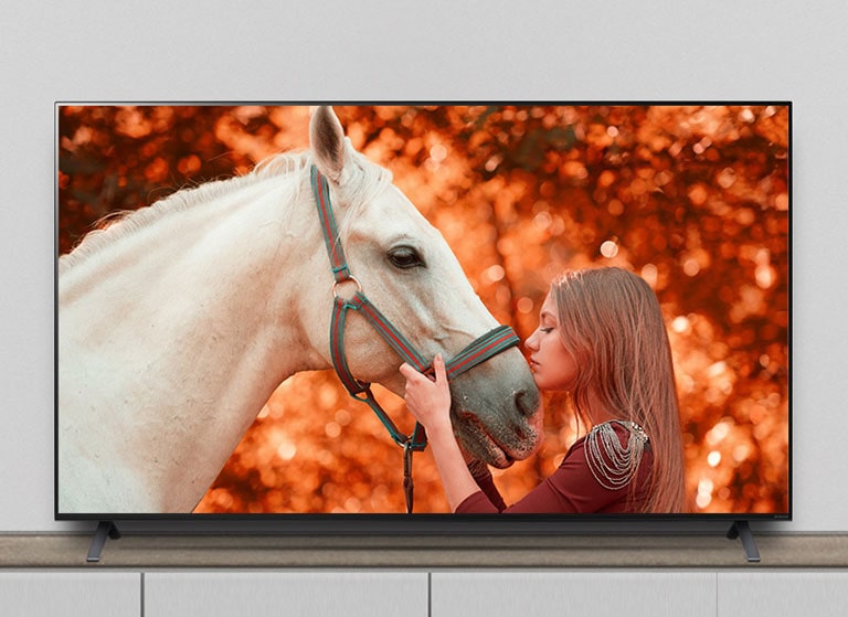 The TV is on the stand, and the screen shows a scene of a movie featuring a horse and a woman.
