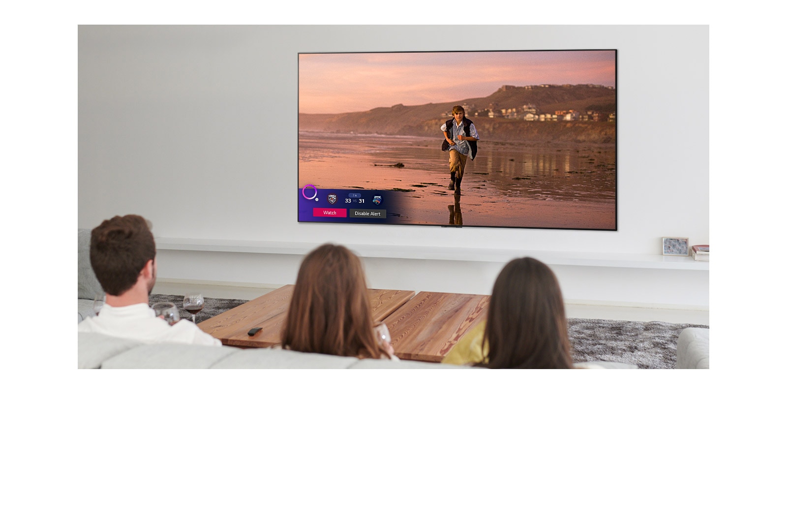 Three people watching TV screen showing a scene from a fantasy movie with a Sports Alert