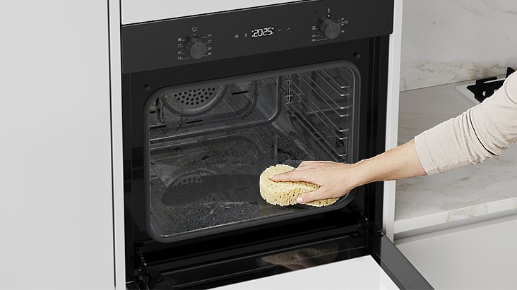 Hand cleaning the interior of a built-in oven with a sponge.