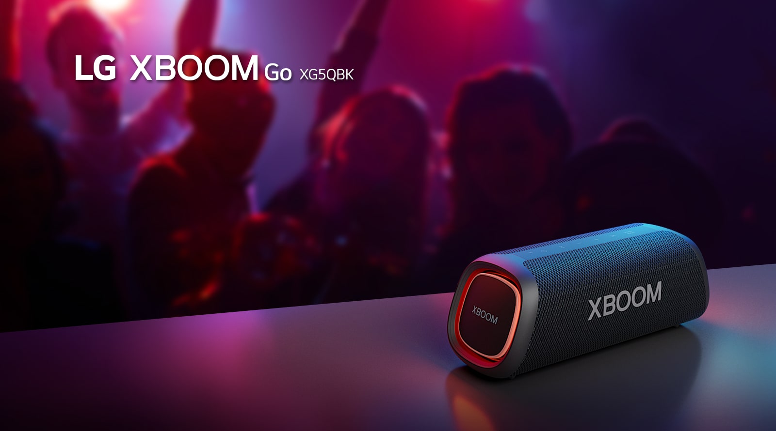 LG XBOOM Go XG5 is placed on the metal table with orange lighting is on. Behind the table, people are enjoying the music.