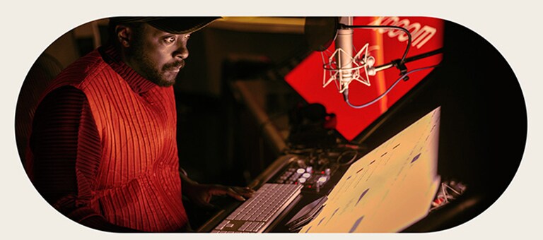 will.i.am is working in studio looking at a screen placed below a mic.	