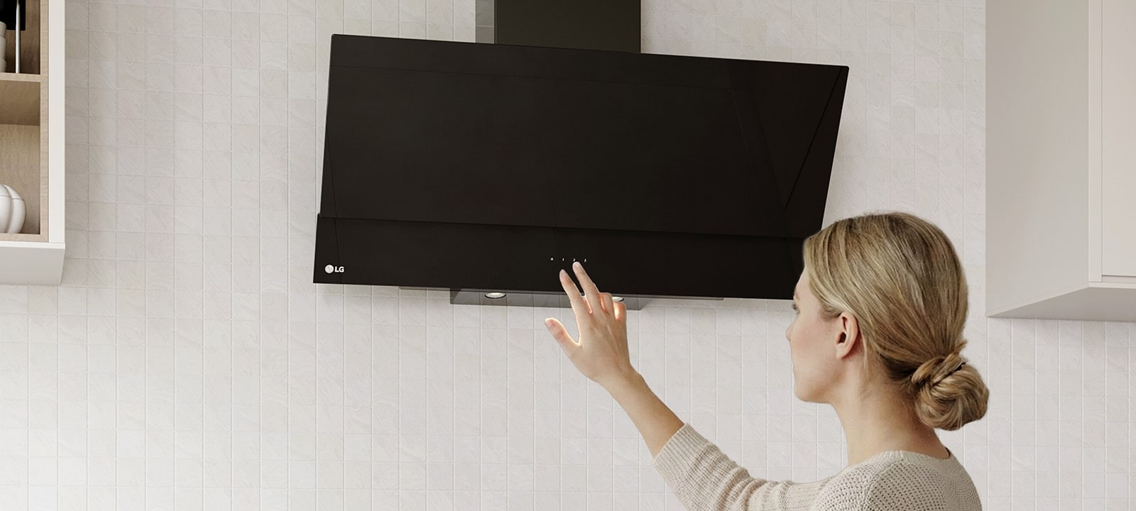 A woman adjusting the touch controls of a black glass hood above a cooktop in a modern kitchen with a white tile wall.