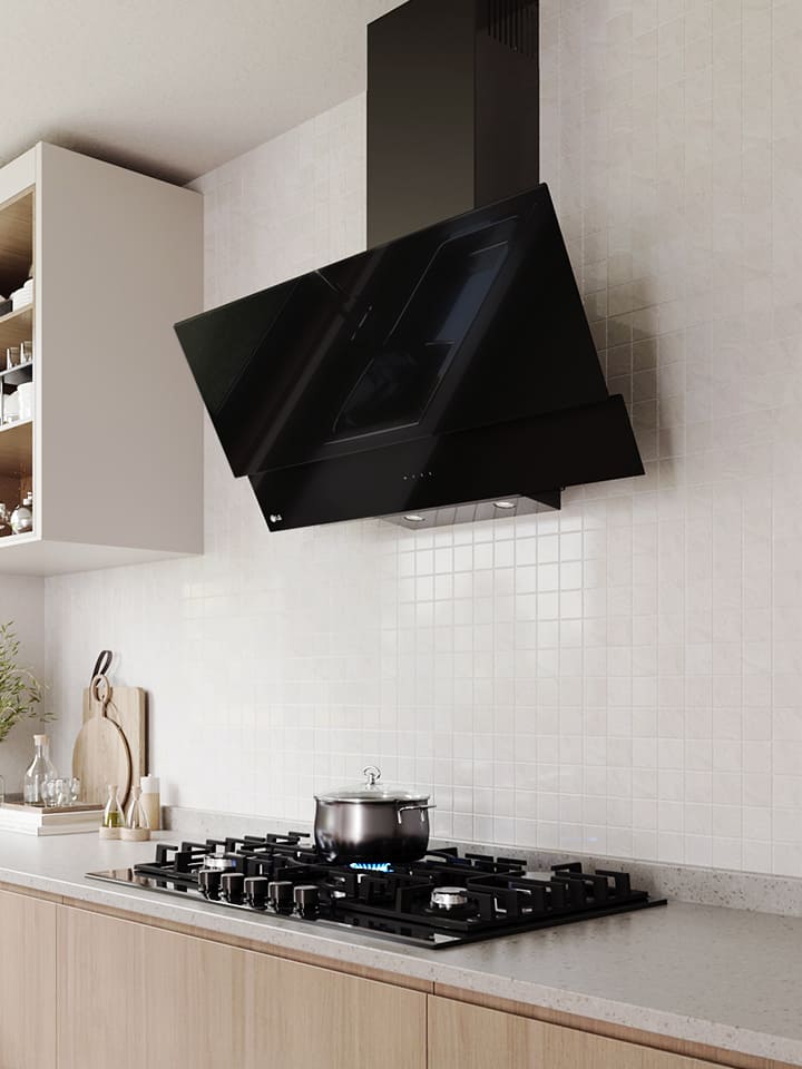 Modern kitchen interior featuring an angled glass hood above a gas cooktop with a pot, against a white tile wall.